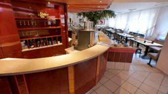 Interior view of Hotel & Metzgerei See featuring a curved reception counter, beverage shelf, and dining area with tables and chairs