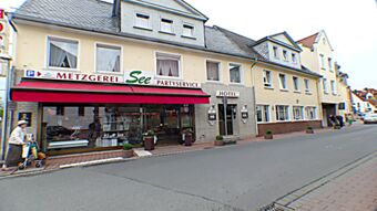Gatebildet av Hotel & Metzgerei See viser en bygning i flere etasjer med slakterbutikk, servering og hotellinngang i en rolig landsby.