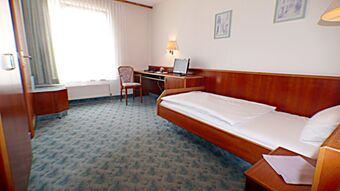 Single hotel room with a bed, desk, chair, small TV, patterned carpet, and wall light at Hotel & Metzgerei See