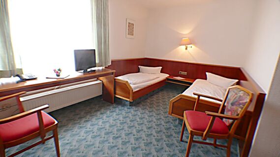 Helles Hotelzimmer mit zwei Einzelbetten, Teppichboden und einem Fernseher im Hotel & Metzgerei See mit Holzvert&auml;felung.