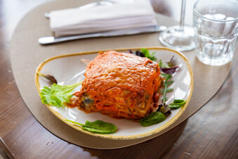 Lasagna topped with tomato sauce and cheese served on a white plate with greens at Bologna Easy Camping Village