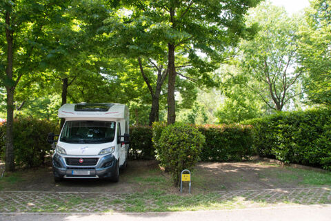 White motorhome parked in a shaded, leafy spot with green bushes and a yellow E 14 sign at Bologna Easy Camping Village