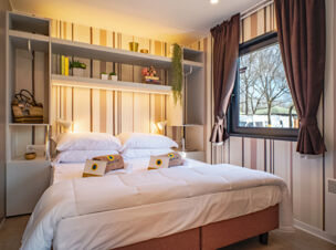 Double bed with white bedding, pillows, towels, and a window with curtains in a room at Bologna Easy Camping Village