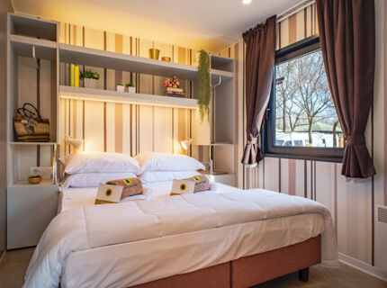 Double bed with white bedding, pillows, towels, and a window with curtains in a room at Bologna Easy Camping Village