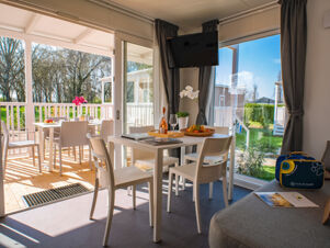 Interior view of a bright dining area with white chairs, a table set with a bottle and fruit basket at Bologna Easy Camping Village