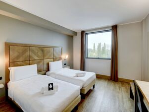 Two single beds with white linens and wooden headboard near a large window in a guest room at B&B Hotel Padova