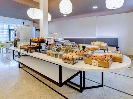 Buffet table in a bright dining area at B&B Hotel Padova with pastries, jars of cereal and nuts, and beverage dispensers on display