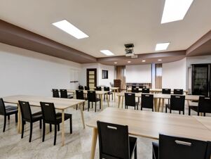 Conference room setup with rectangular wooden tables and black chairs under ceiling lights at B&B Hotel Padova