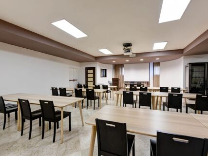 Conference room setup with rectangular wooden tables and black chairs under ceiling lights at B&B Hotel Padova