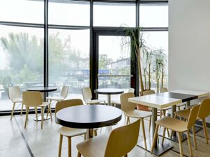 Dining area with wooden chairs, round and square black and white tables, large windows, and plants at B&B Hotel Padova