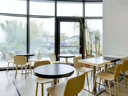 Dining area with wooden chairs, round and square black and white tables, large windows, and plants at B&B Hotel Padova