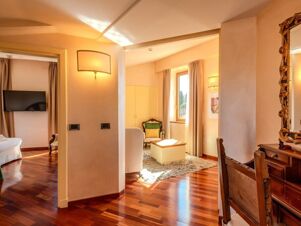 Sunlit room at B&B Hotel Firenze Pitti Palace al Ponte Vecchio with wooden floors, armchairs, mirror, and flat screen TV visible