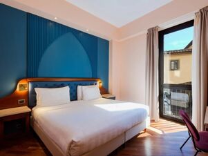 Bedroom with large bed featuring white linens, wood and blue headboard, nightstands, window with curtains at B&B Hotel Firenze Pitti Palace al Ponte Vecchio