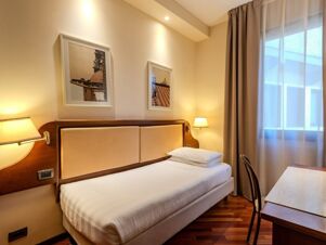 Single bed with white linens and pillows next to wooden desk and chair in B&B Hotel Firenze Pitti Palace al Ponte Vecchio room