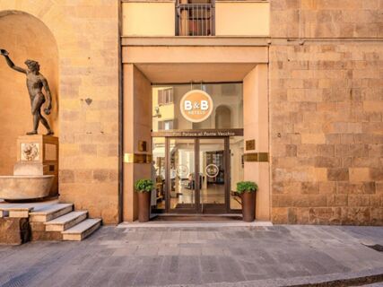 Entrance to B&B Hotel Firenze Pitti Palace al Ponte Vecchio with glass doors, two potted plants, and a bronze statue nearby