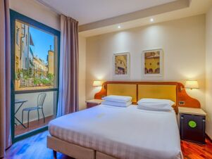 A hotel room at B&B Hotel Firenze Pitti Palace al Ponte Vecchio with a double bed, bedside tables, lamps, and balcony door showing outdoor buildings