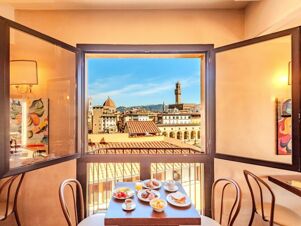 Table with breakfast plates and drinks by open window showing cityscape and historic towers at B&B Hotel Firenze Pitti Palace al Ponte Vecchio