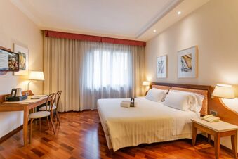 Hotel bedroom at B&B Hotel Firenze Pitti Palace al Ponte Vecchio with a double bed, wooden desk, chairs, lamps, and window curtains