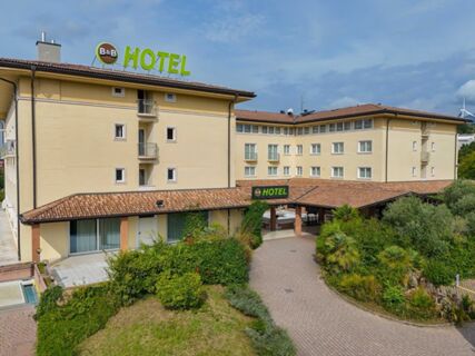 Beige multi-story building with a tiled roof and greenery around the entrance at B&B Hotel Affi Lago di Garda