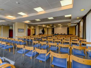 Conference room with rows of wooden chairs with blue seats facing a presentation area at B&B Hotel Affi Lago di Garda