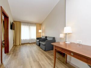 Room in B&B Hotel Affi Lago di Garda with wooden floor, two gray armchairs, a wooden desk with lamp, and window with curtains