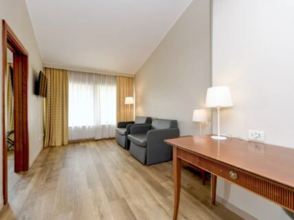 Room in B&B Hotel Affi Lago di Garda with wooden floor, two gray armchairs, a wooden desk with lamp, and window with curtains