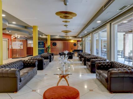 Spacious lounge area at B&B Hotel Affi Lago di Garda with brown leather sofas, glass tables, and large windows showing outdoor seating