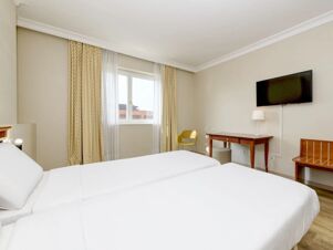 Two single beds with white bedding are in a hotel room at B&B Hotel Affi Lago di Garda with a window, desk, TV, chair, and bench