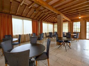 Dining area with round tables and blue patterned chairs under a wooden ceiling at B&B Hotel Affi Lago di Garda