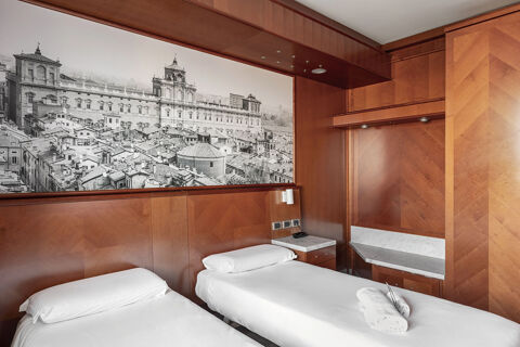 Two single beds with white linens and rolled towels in a wooden room featuring a large black and white cityscape at B&B Hotel Modena