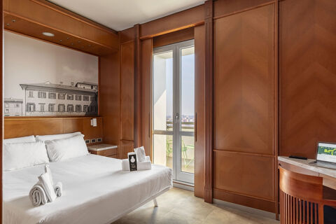 Hotel room at B&B Hotel Modena with white bed linens, wooden walls, balcony doors, and a desk with a laptop