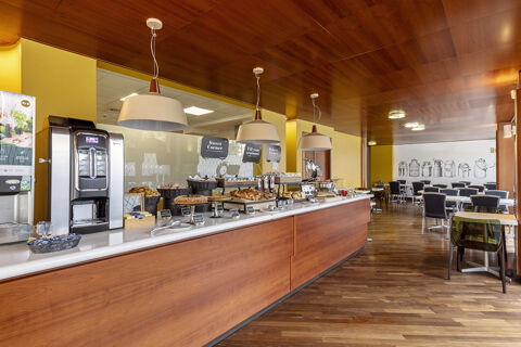 Breakfast buffet with pastries, croissants, coffee machine, and dining area with tables and chairs at B&B Hotel Modena