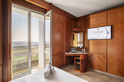 Bedroom at B&B Hotel Modena with wooden furnishings, a desk with laptop, wall-mounted TV, and balcony with green table and chair