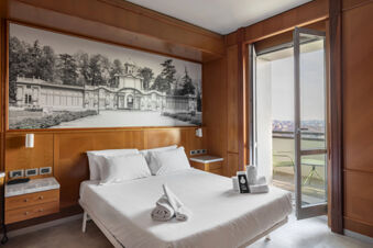 Modern hotel room at B&B Hotel Modena with a large bed, wood-paneled walls, black and white photo above the bed, and balcony with chairs
