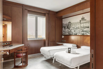 Twin beds with white linens and folded towels in a wood-paneled room with a desk and window at B&B Hotel Modena