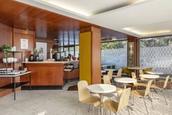 Dining area with round white tables and wooden chairs next to a wooden buffet counter at B&B Hotel Modena