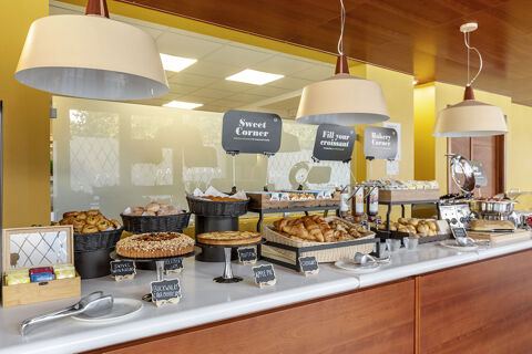 Breakfast buffet with various pastries, croissants, jams, and baked goods displayed under hanging lamps at B&B Hotel Modena
