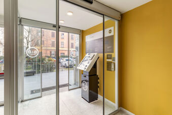 Indoor check-in kiosk with touchscreen and information board inside a glass entrance area at B&B Hotel Modena