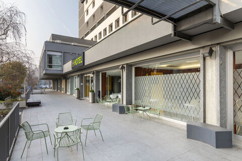 Outdoor seating area with metal tables and chairs along the building exterior of B&B Hotel Modena showing the hotel entrance and windows