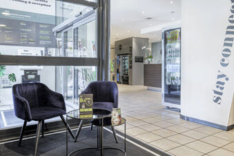 Two black chairs and two small round tables in the lobby area of B&B Hotel Bologna with vending machines and a reception desk visible in the background