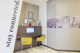 Two yellow chairs and a computer desk with a monitor displaying Google at B&B Hotel Bologna business corner