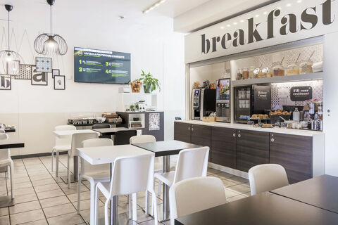 Dining area with white and black chairs and tables in B&B Hotel Bologna breakfast room with cereal dispensers and coffee machines
