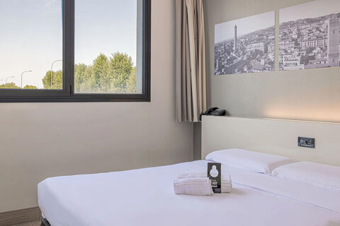 Bright hotel room at B&B Hotel Bologna with a large bed, folded white towels, telephone, and black and white wall art