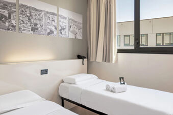 Minimalist twin bed setup at B&B Hotel Bologna with white linens, folded towels, a telephone, and a large window with curtains
