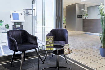 Two black armchairs with a glass table between them and a tiled floor in the B&B Hotel Bologna lobby area