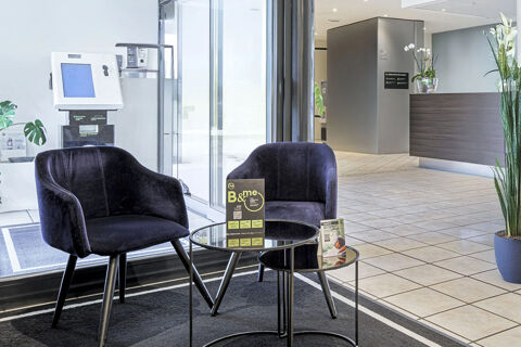 Two black armchairs with a glass table between them and a tiled floor in the B&B Hotel Bologna lobby area