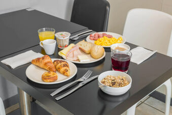 Breakfast spread with croissants, bread, cheese, eggs, cold cuts, cereal, yogurt, orange juice, and coffee at B&B Hotel Bologna