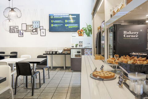 Bakery Corner with croissants, cake, and yogurt on a counter, tables, chairs, and a TV screen in B&B Hotel Bologna dining area
