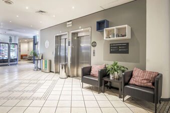 Lobby area of B&B Hotel Bologna with two black armchairs, striped pillows, a small table with plant, and two elevator doors