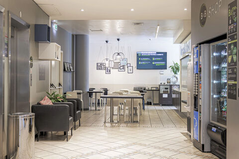 Seating area with tables, chairs, vending machines, an elevator, and wall decorations in B&B Hotel Bologna lobby